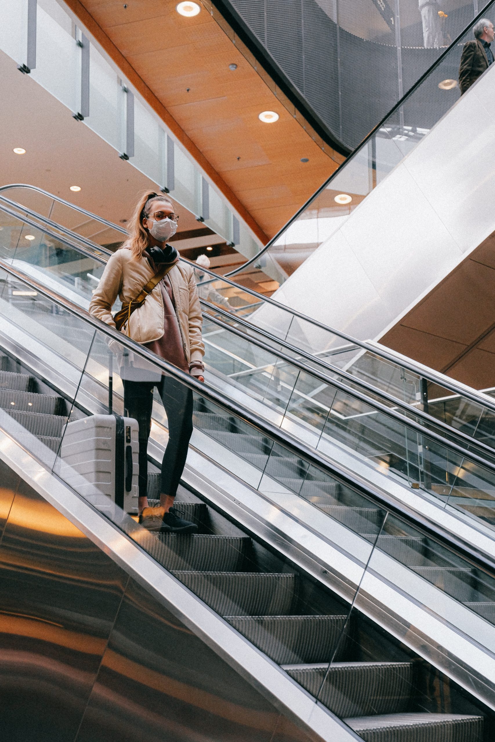 woman on an escalator with suitcase in an airport covid